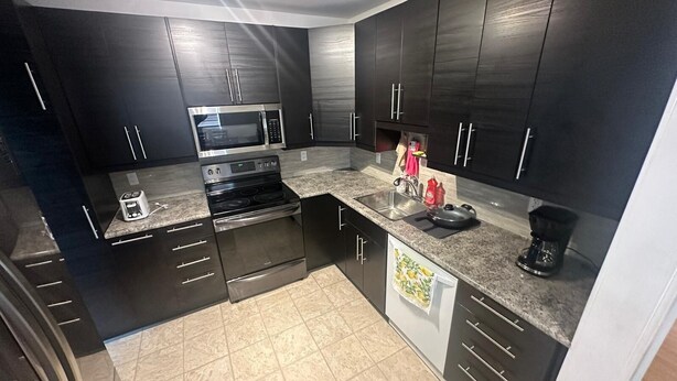 A modern kitchen with dark cabinetry, stainless steel appliances, and a granite countertop.