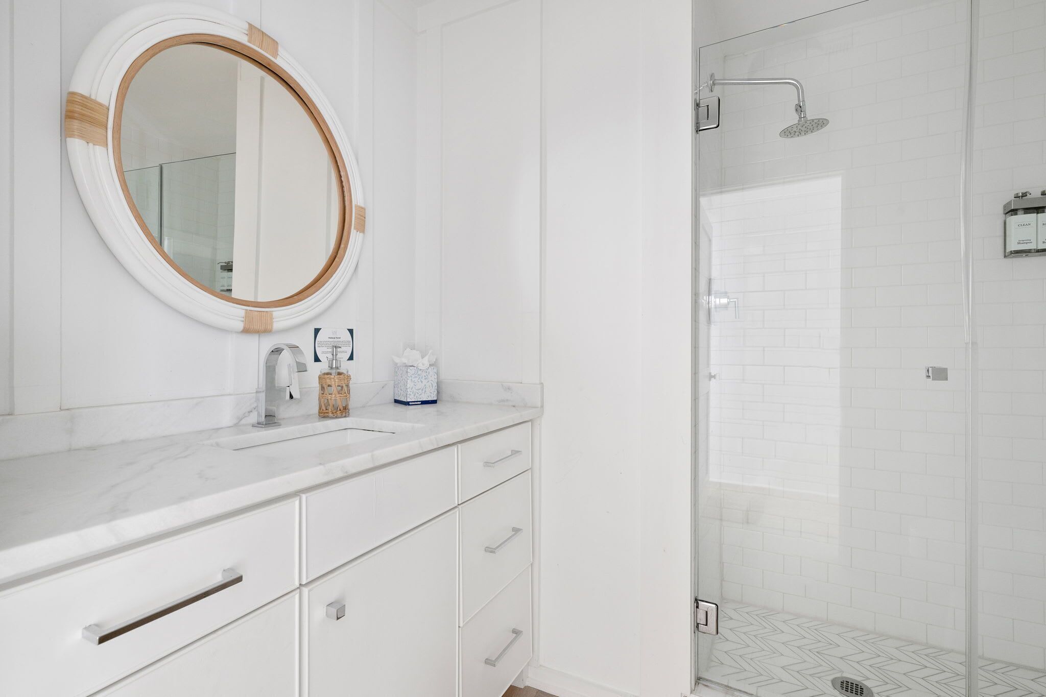 Une salle de bain moderne avec un meuble-lavabo blanc, un miroir rond et un espace douche doté d’une porte en verre.