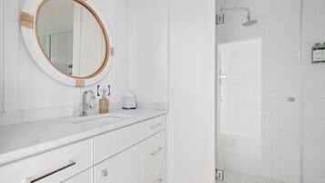 Une salle de bain moderne avec un meuble-lavabo blanc, un miroir rond et un espace douche doté d’une porte en verre.