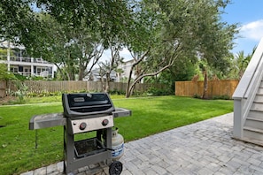 A backyard with a barbecue grill, a paved patio, and a wooden fence.