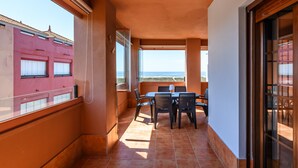 Un balcón con mesa y sillas, vista al mar y un edificio en el fondo.
