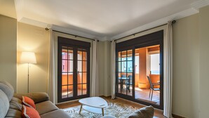 Una sala de estar con un sofá, una mesita y una lámpara. Amplias puertas correderas de vidrio dan a un patio al aire libre.