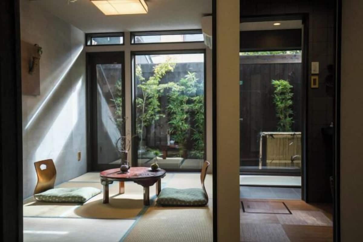 A traditional Japanese room with tatami flooring, a low table with a tea set, and a view of a garden through large sliding doors.
