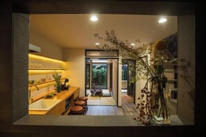 Una cucina moderna con isola centrale, un'area pranzo con sgabelli e vista su un giardino tramite una porta in vetro.