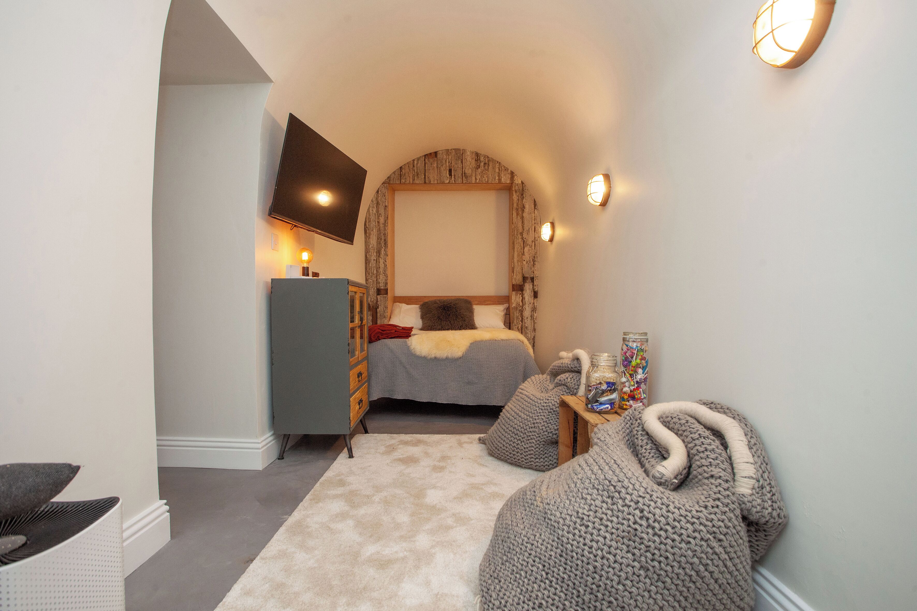 A cozy bedroom with a bed, a dresser, a TV mounted on the wall, and a small table with snacks.