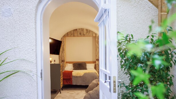 A bedroom with a bed, a bedside table, a lamp, and a plant. - Higgihaus Apt1 36 37 Royal York Cres (Bristol)