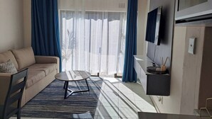 A living room with a sofa, a small round table, a TV mounted on the wall, and a window with curtains. - Hazel Haven 2 Guest House (Pretoria)