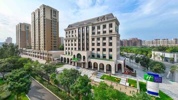 A modern hotel with a central courtyard, multiple floors, and a prominent green sign.
