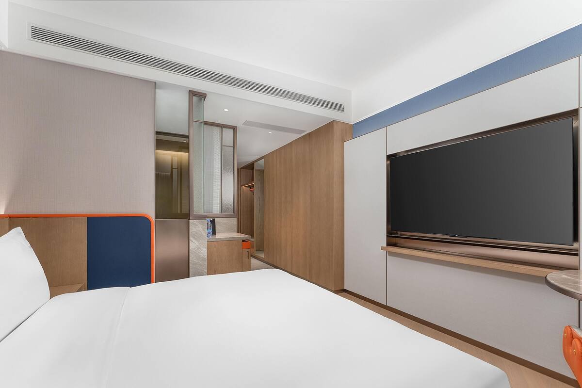 Moderni hotellihuone, jossa on suuri sänky, televisio, kylpyhuone ja yksi seinä on koristeltu puupaneloinnilla.
