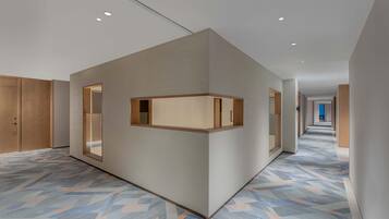 A modern hotel corridor with a geometric patterned floor, wooden paneling on the walls, and recessed ceiling lights.