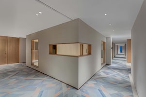 Un pasillo de hotel moderno con un suelo de diseño geométrico, paneles de madera en las paredes y luces empotradas en el techo.
