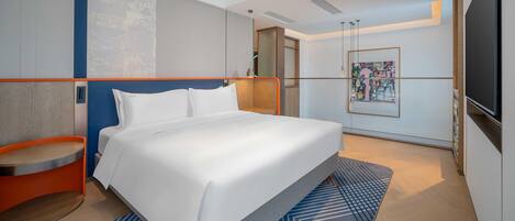 Una habitación de hotel moderna con una cama grande, un pequeño rincón de descanso, un televisor y un cuadro en la pared.