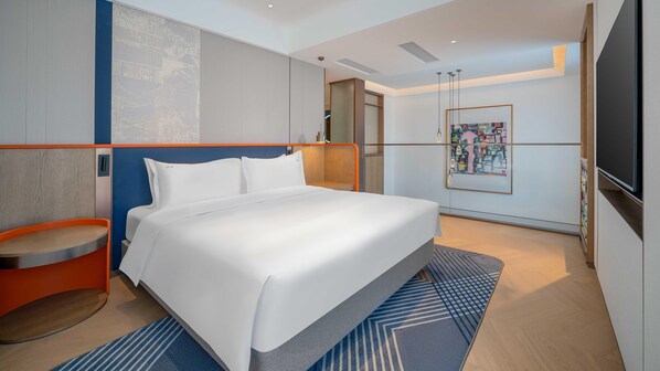 A modern hotel room with a large bed, a small seating area, a TV, and a painting on the wall.