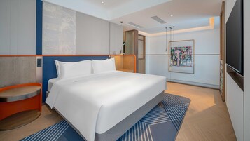Una habitación de hotel moderna con una cama grande, un pequeño rincón de descanso, un televisor y un cuadro en la pared.