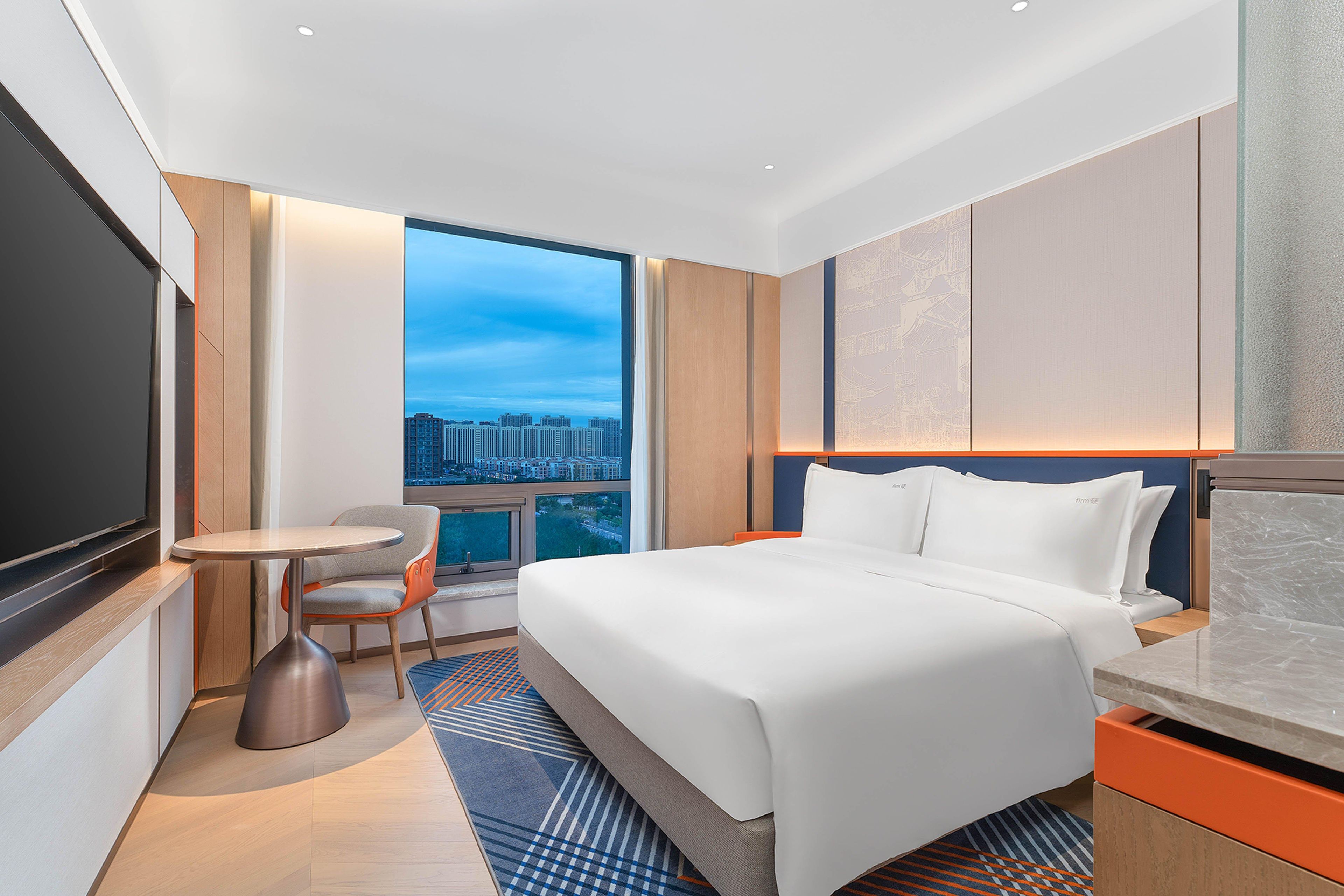 Una habitación de hotel moderna con una cama grande, un escritorio, una silla y un televisor.