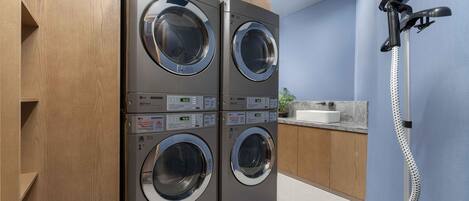 A laundry room with two stacked front-loading washing machines and a hose reel.