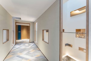 Un pasillo moderno de hotel con suelo estampado, ventanas de madera y luces empotradas.