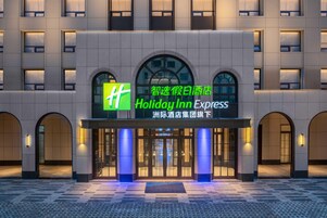 Fachada de un hotel Holiday Inn Express con señalización iluminada, entradas arqueadas y un primer piso con azulejos.