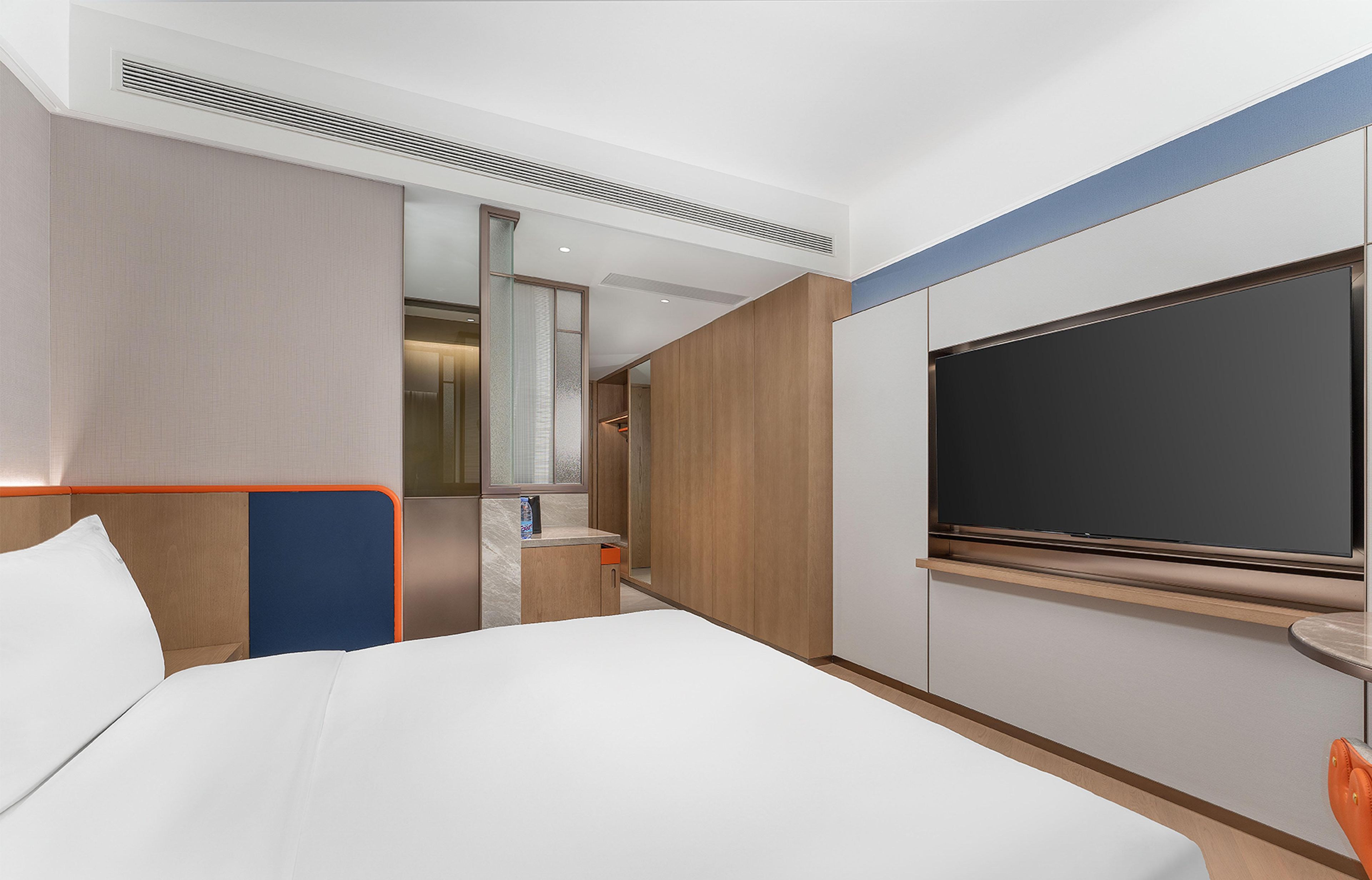 Una habitación de hotel moderna con una cama grande, televisor, baño y un revestimiento de pared de madera.
