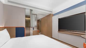 Una habitación de hotel moderna con una cama grande, televisor, baño y un revestimiento de pared de madera.