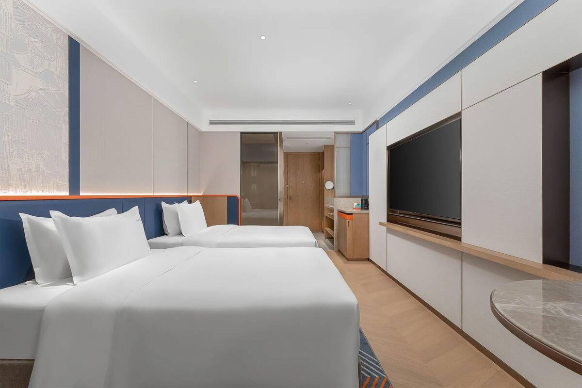 Hotellihuone, jossa on kaksi sänkyä, televisio ja pieni keittonurkkaus.