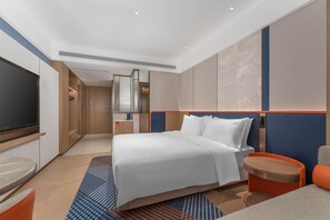Una habitación de hotel moderna con una cama grande, un televisor, un escritorio y una zona de estar.