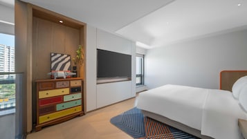Habitación de hotel moderna con una cama grande, un aparador colorido, un televisor de pantalla plana y una ventana con vistas a edificios.