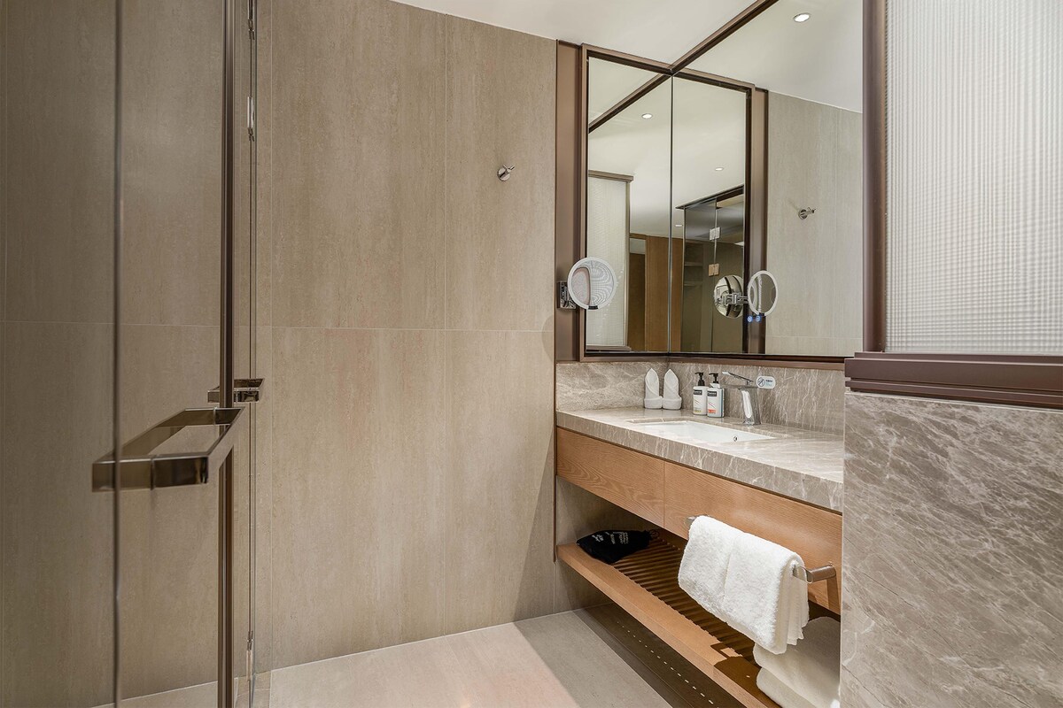 A modern bathroom with a glass shower enclosure, a wooden vanity with a marble countertop, and a large mirror above the sink.