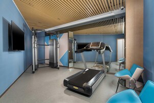 Un gimnasio moderno con cinta de correr, máquinas de pesas y sillas de ejercicio.
