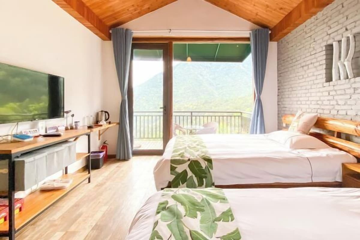 Une chambre dotée de deux lits, d’un bureau, d’une télévision et d’un balcon offrant une vue sur la montagne.