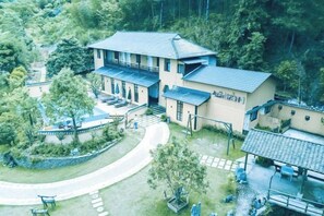 A two-story building with a balcony, surrounded by greenery and a paved walkway.