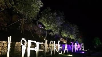 Illuminated letters spelling "FLIKE TRAVEL" against a stone wall, surrounded by trees.