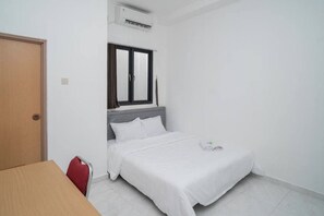 Una habitación pequeña y limpia con una cama, una ventana y una mesa.