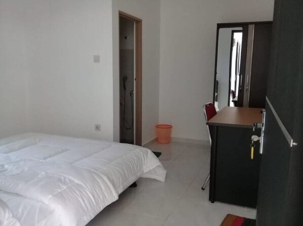 A bedroom with a bed, a small desk, a mirror, and a shower area. - Hotel O Mahagoni House Syariah (Bogor)