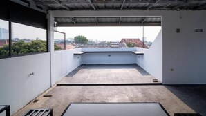 A rooftop terrace with a concrete floor, metal roof, and a view of buildings and trees. - Hotel O Mahagoni House Syariah (Bogor)