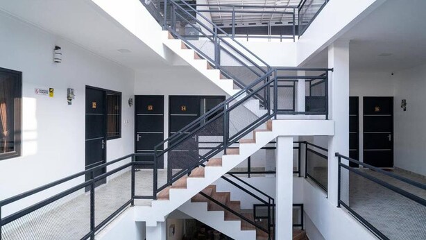 A multi-level interior with a central staircase, white walls, and black doors. - Hotel O Mahagoni House Syariah (Bogor)