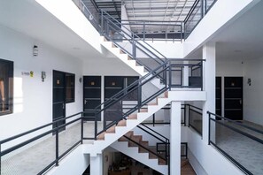 Un intérieur à plusieurs niveaux, avec un escalier central, des murs blancs et des portes noires.