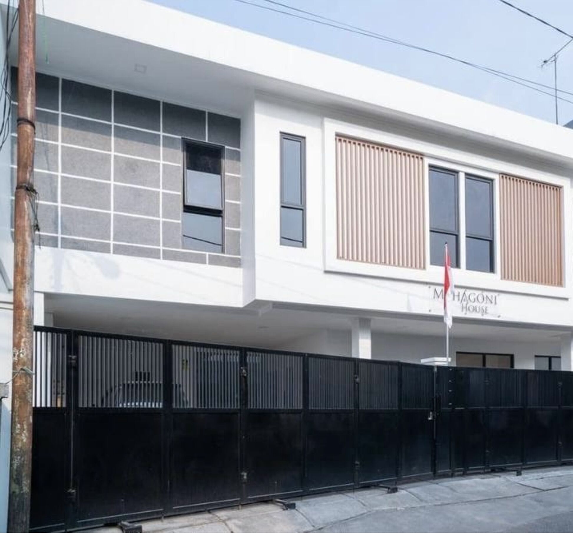 Un bâtiment moderne à la façade blanche, doté de grandes fenêtres et d’une enseigne indiquant « M. HAGONI HOUSE ».