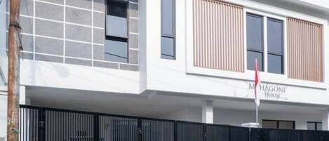 Un bâtiment moderne à la façade blanche, doté de grandes fenêtres et d’une enseigne indiquant « M. HAGONI HOUSE ».
