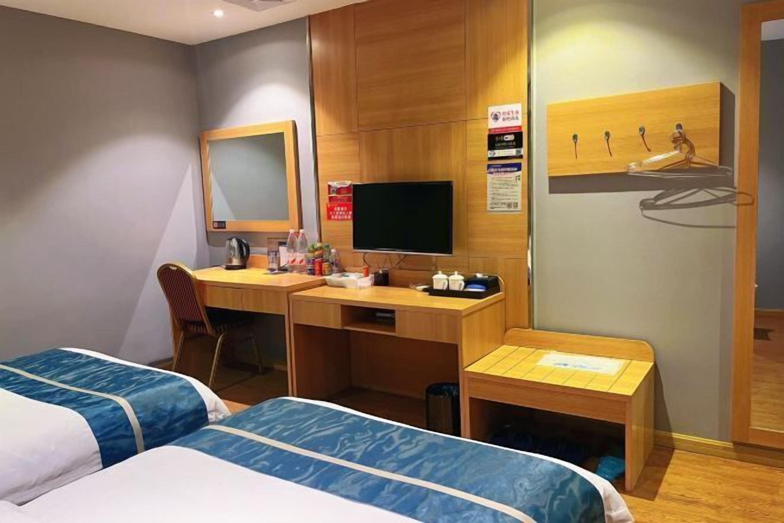 A hotel room with two beds, a desk, a chair, a television, and a wooden wall panel.