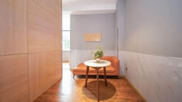 A narrow hallway with a round table and a plant, wooden paneling on the walls, and a view into another room.