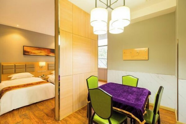 A hotel room with a bed, a dining table with chairs, and a painting on the wall.