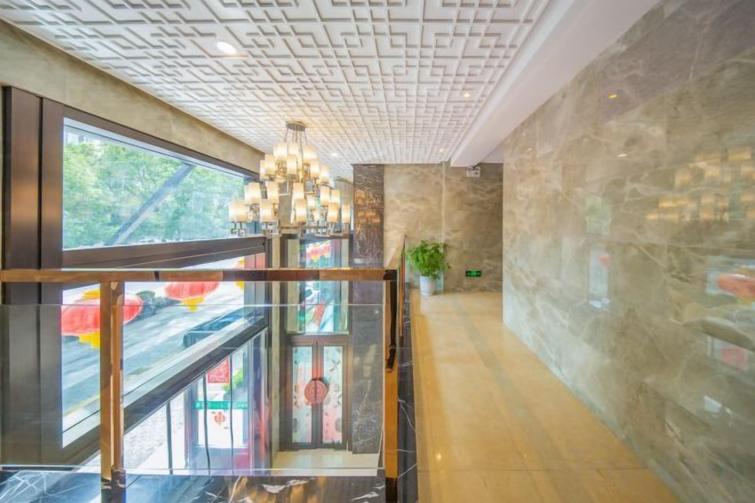 Un hall d’hôtel avec un ascenseur en verre, un lustre et un mur en pierre.