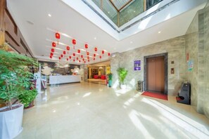 Ένα ξενοδοχειακό λόμπι με έναν πάγκο υποδοχής, μια σκάλα και ένα κόκκινο χαλί που οδηγεί σε έναν ανελκυστήρα.