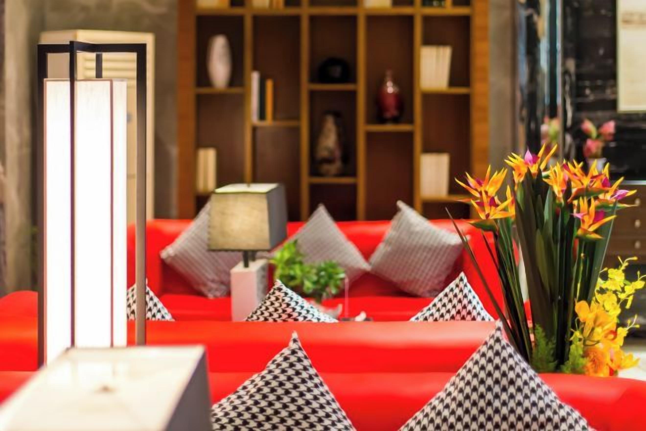 A hotel lobby with red seating, a bookshelf, and a lamp.