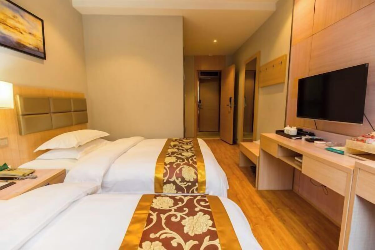 A hotel room with two beds, a desk, a television, and a door leading to another room.