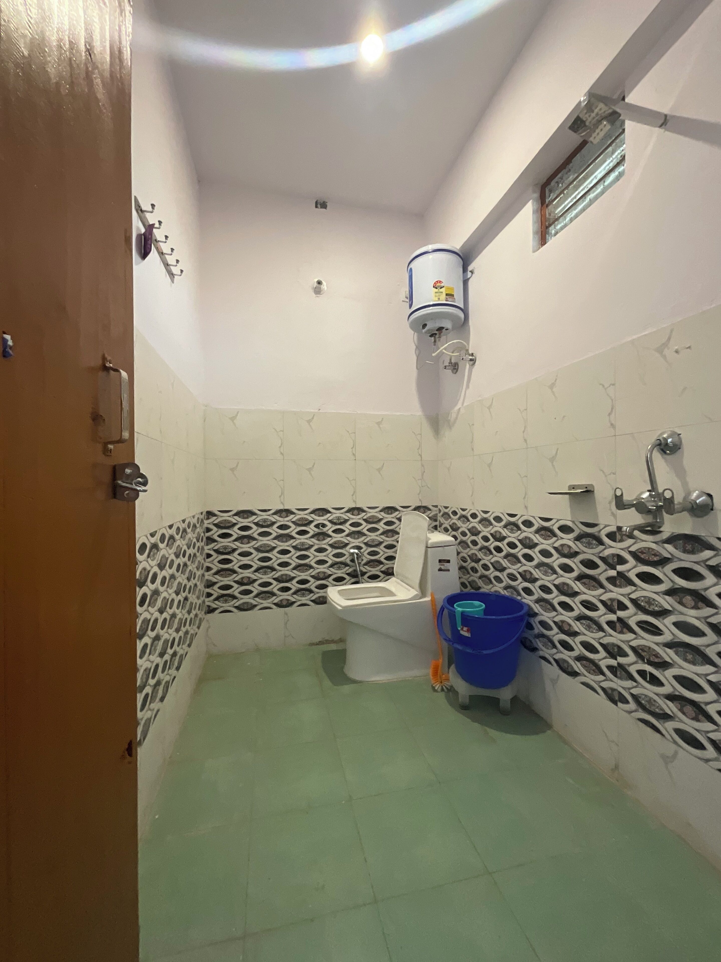 A bathroom with a toilet, a blue bucket, and a water heater mounted on the wall.