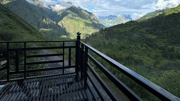Eine Holzterrasse mit Geländer, mit Blick auf eine gebirgige Landschaft unter wolkenlosem Himmel.