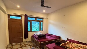 Ein Zimmer mit einem gemusterten Boden, einem Bett mit roter Decke, einem Sofa mit floralem Bezug, einem Deckenventilator und einem Fenster mit Vorhängen.