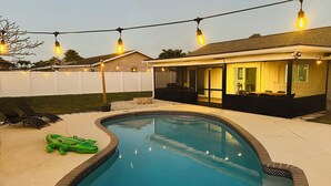 Un patio trasero con piscina, terraza techada y luces colgantes.